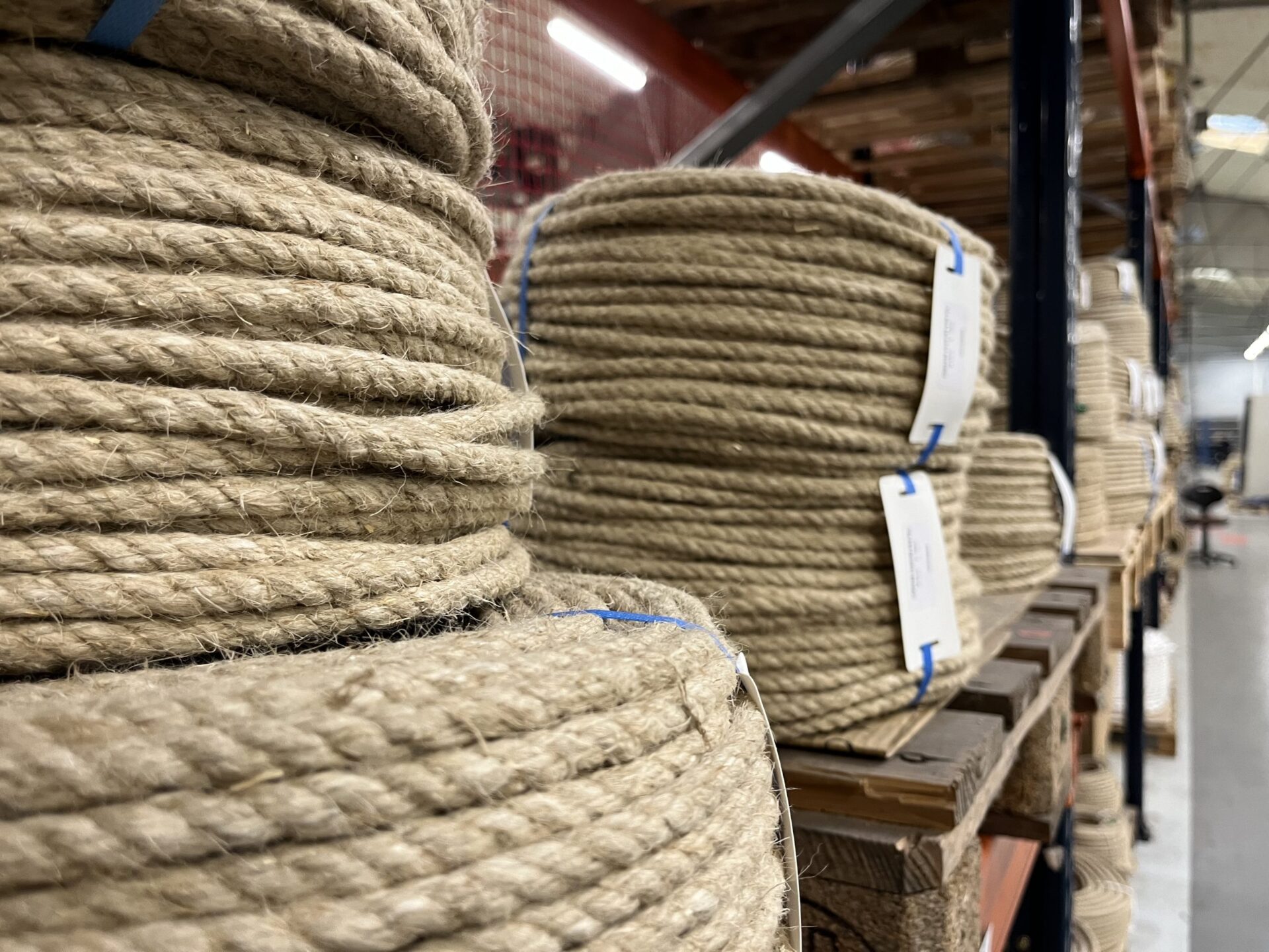 Bobines de grosses cordes en chanvre ou en jute, soigneusement enroulées et attachées avec de la ficelle blanche, posées au sol dans ce qui semble être un atelier ou une sellerie.