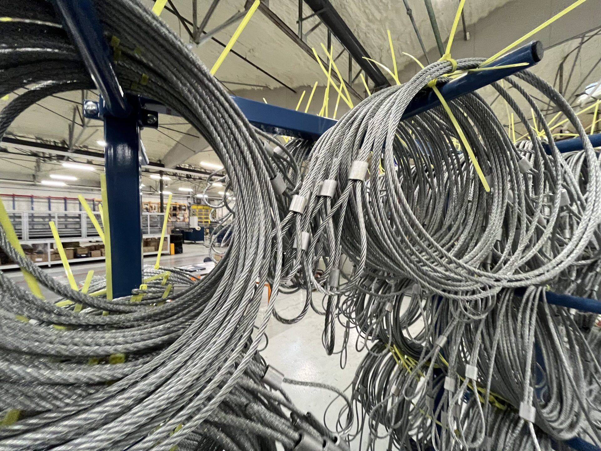 Boucles de câbles métalliques en acier, suspendues et rangées sur des supports dans un atelier industriel.